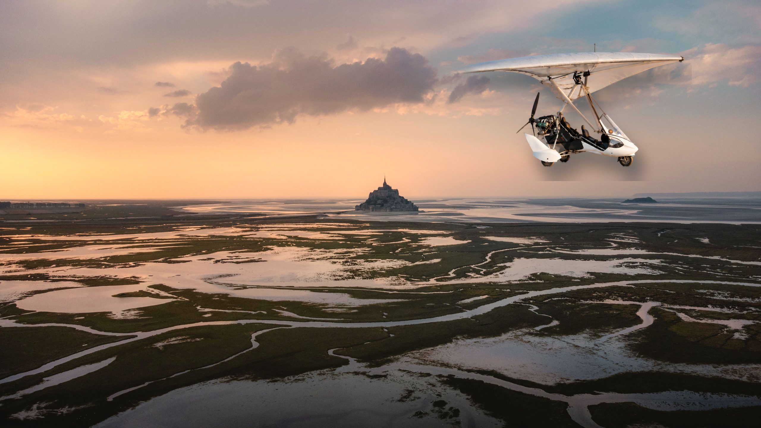 Un ULM en vol au-dessus de la baie du Mont-Saint-Michel au coucher du soleil